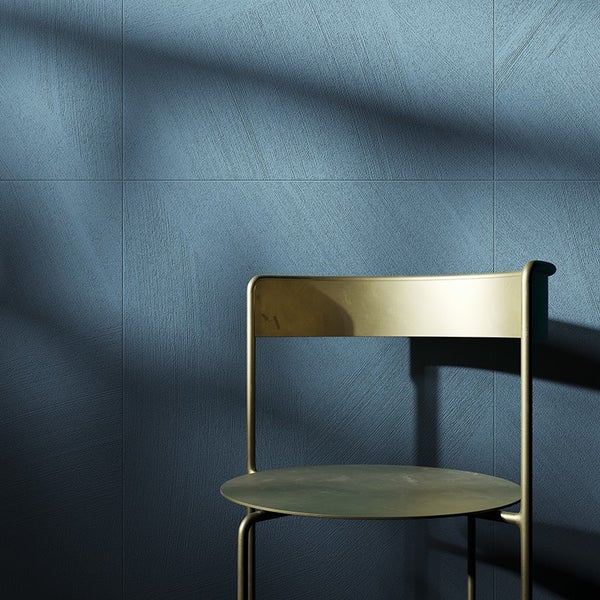 Wandfliesen mit strukturierter Oberfläche in quadratischer Verlegung vor einem metallischen Stuhl in einem modern gestalteten Raum.