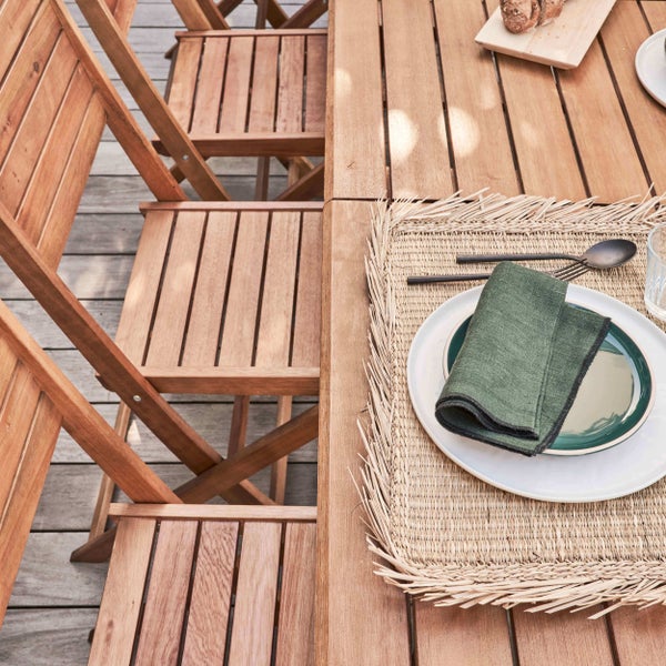 Gedeckter Gartentisch aus Holz mit passenden Klappstühlen auf einer Terrasse aus Holzdielen.