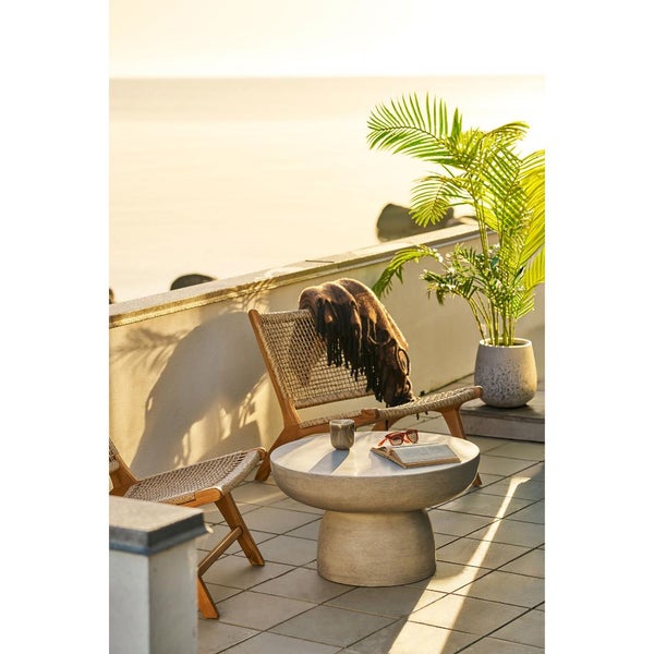 Moderne Terrasse mit zwei Holz-Lounge-Sesseln mit Geflecht, einem runden Couchtisch in Betonoptik und einer grossen Topfpalme mit Blick auf das Wasser