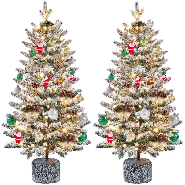 Zwei schneebedeckte Weihnachtsbäume mit Ornamenten und Lichtern auf Baumstumpffuß