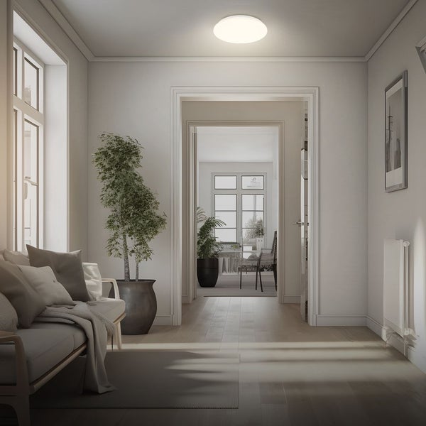Flache, runde LED-Deckenleuchte in einem hellen, modern eingerichteten Raum mit Sofa, Zimmerpflanze und Holzfußboden.