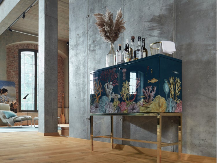 Moderner Barschrank mit Korallenriff-Design auf Metallbeinen in einem hellen Industrieraum mit Betonwänden und Holzboden.