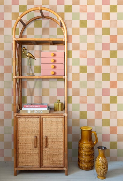 Regal aus Rattan mit Dekorationsobjekten wie einer Vogel-Figur, Büchern und Vasen vor einer Wand mit Karomuster