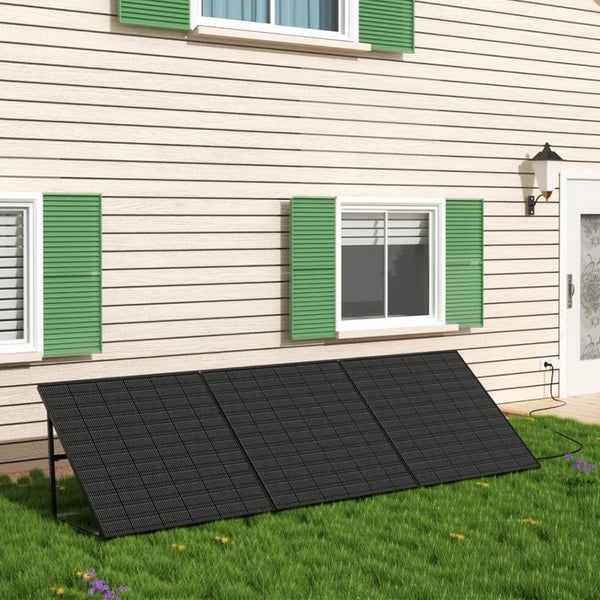 Drei Solarpaneele auf einer Rasenfläche vor einer Hauswand mit Fenstern, Fensterläden und einem Anschlusskabel.