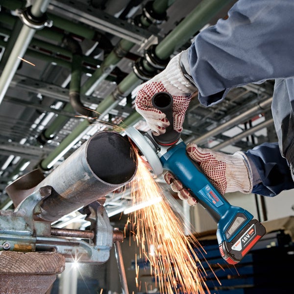 Bosch Professional 18 Volt Akku-Winkelschleifer bearbeitet ein Metallrohr in einem Schraubstock mit Funkenflug.