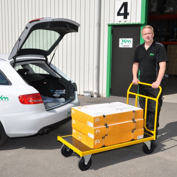 Mann mit Plattformwagen vor Lager und Auto