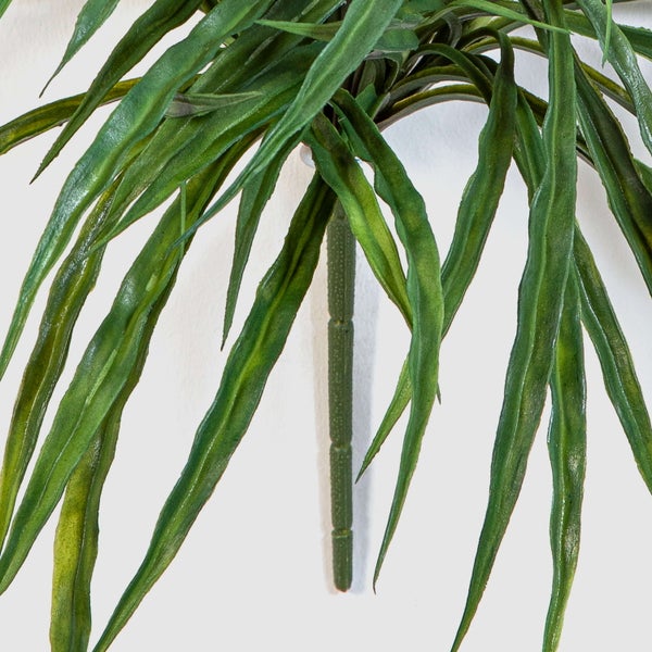 Detailaufnahme einer künstlichen Dracaena Pflanze mit langen grünen Blättern und einem strukturierten Stiel.
