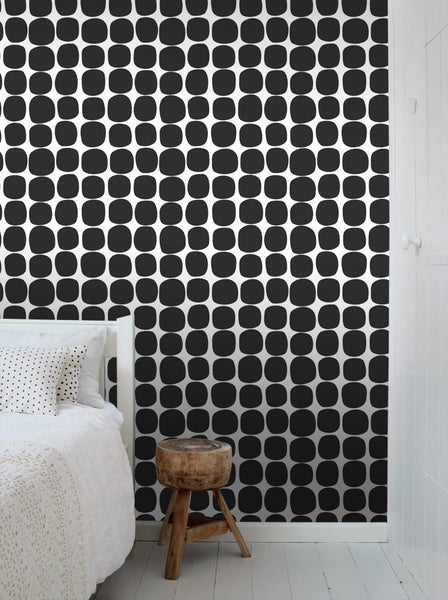 Schlafzimmer mit Bett, Hocker und Tapete mit Muster aus schwarzen, abgerundeten Quadraten