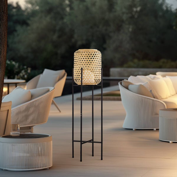 Moderne Outdoor-Lounge bei Dämmerung mit hohem schwarzen Laternenständer aus Metall, Flechtsesseln und Sofas auf einer weitläufigen Terrasse.