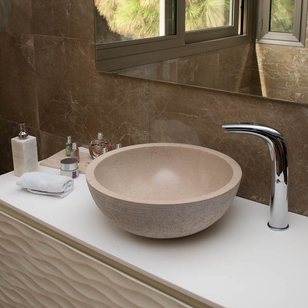 Modernes Badezimmer mit rundem Naturstein-Waschbecken, Chrom-Armatur und weißer Waschtischplatte vor braunen Marmoroptik-Fliesen.