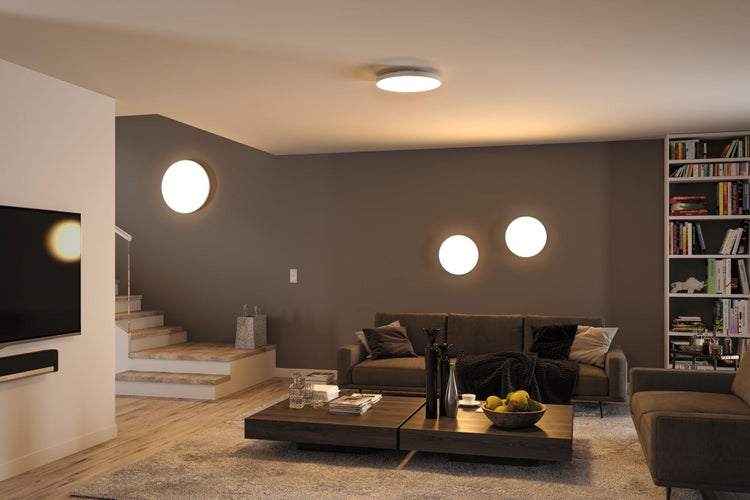 Modernes Wohnzimmer mit runden LED-Decken- und Wandleuchten, einem grauen Sofa, Couchtischen aus Holz und einem gut gefüllten Bücherregal.