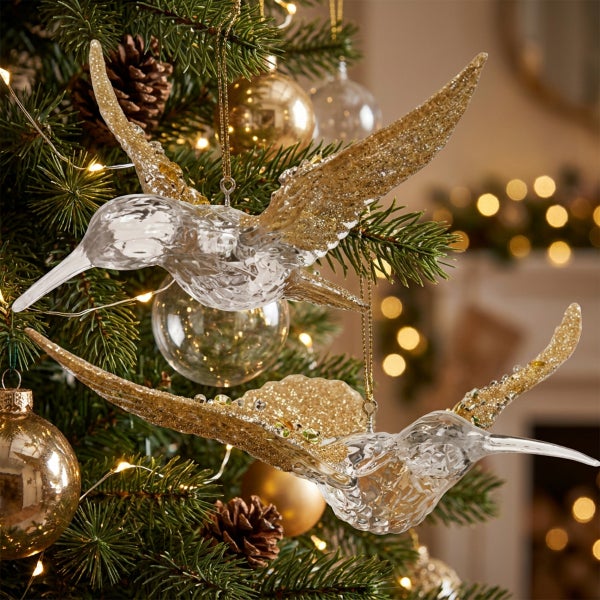 Zwei dekorative Kolibris als Weihnachtsbaumschmuck aus Glas mit Details in Glitzeroptik an einem geschmückten Weihnachtsbaum.