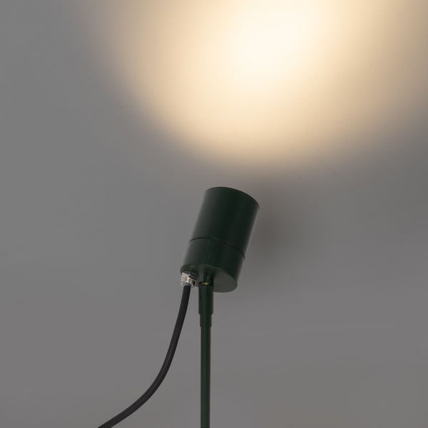 Dunkelgrüner Gartenstrahler mit Erdspieß und nach oben gerichtetem warmweißem Lichtstrahl.