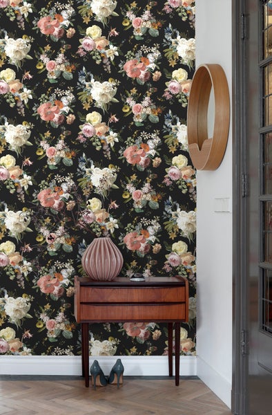 Ein Zimmer mit einer Wandtapete mit Blumenmuster, einem Holztisch und einem runden Spiegel.