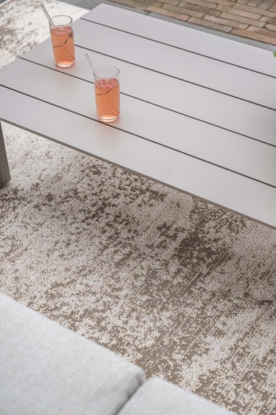 Outdoor-Teppich mit Vintage-Muster unter einem grauen Gartentisch auf einer Terrasse.