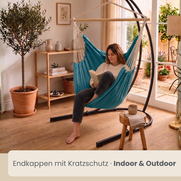 Eine Frau sitzt in einem Hängesessel mit Gestell in einem hellen Wohnraum mit Blick auf eine Terrasse, mit Endkappen mit Kratzschutz ausgestattet.