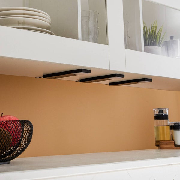 Drei schwarze LED-Unterbauleuchten montiert unter einem weißen Küchenwandschrank.