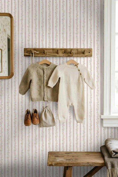 Tapete mit vertikalem Streifenmuster und floralen Ranken in einem hellen Kinderzimmer mit Holzgarderobe und Babykleidung.