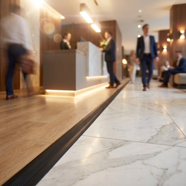 Übergangsprofil zwischen Holzoptik Boden und Marmorfliesen in einem modern gestalteten Hotelfoyer mit Empfangsbereich und Personen im Hintergrund.