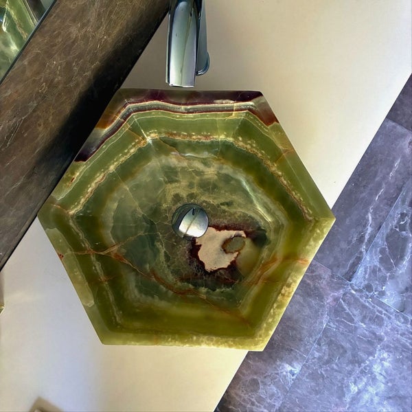 Sechseckiges Aufsatzwaschbecken aus Onyx-Naturstein mit verchromter Armatur und Ablauf auf einer hellen Arbeitsplatte.