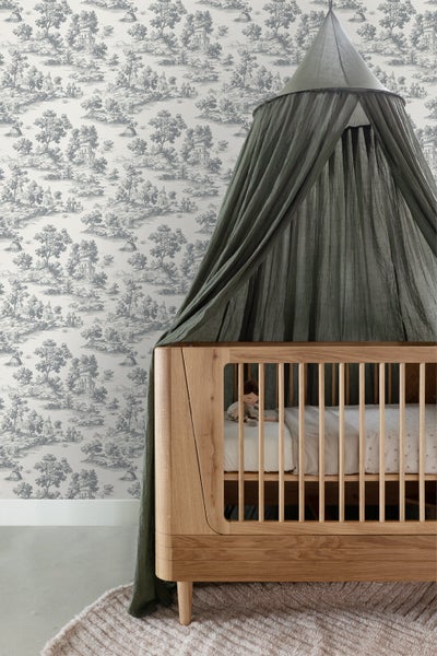 Kinderzimmer mit Holz-Babybett, dunkelgrünem Baldachin und Vliestapete mit Toile-de-Jouy-Landschaftsmuster in Graugrün.