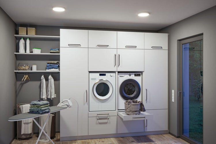 Ein moderner Hauswirtschaftsraum mit weißen Schränken, Waschmaschine, Wäschetrockner, Bügelbrett und offenen Regalen.