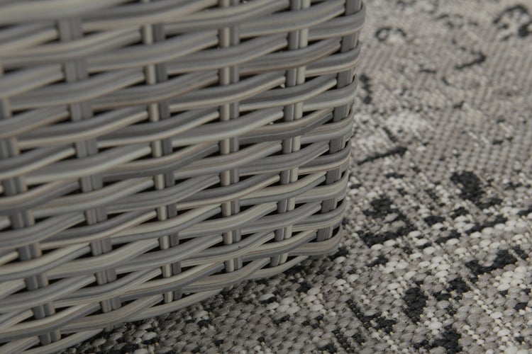 Nahaufnahme eines Polyrattan-Geflechts von Gartenmöbeln auf einem gemusterten Outdoor-Teppich.