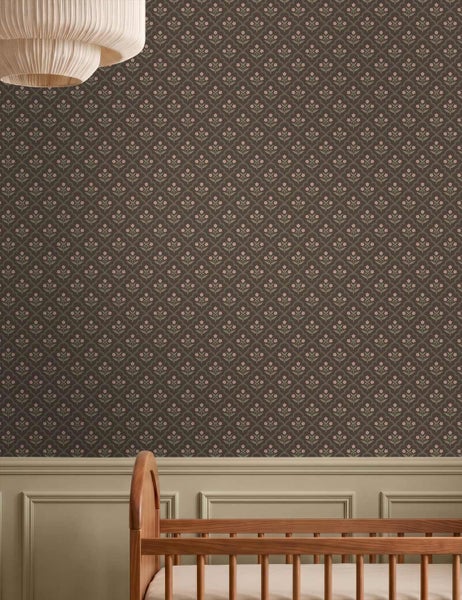 Kinderzimmerwand mit floral gemusterter Tapete über dekorativer Wandvertäfelung, mit einem hölzernen Gitterbett und einer Plissee-Lampe.