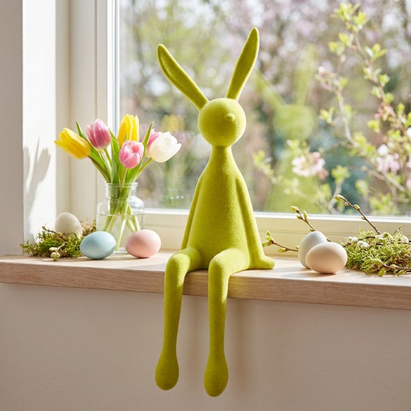 Osterdekoration bestehend aus einer sitzenden Hasenfigur auf einer Fensterbank mit Tulpen in einer Glasvase und Ostereiern als Frühlingsdeko.