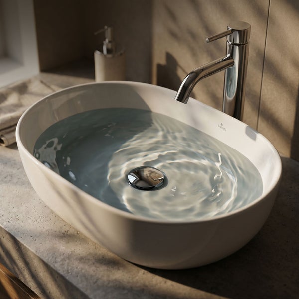Ovale Aufsatzwaschschale aus Keramik mit Wasser gefüllt, inklusive verchromter Armatur auf einer Ablage in Betonoptik.