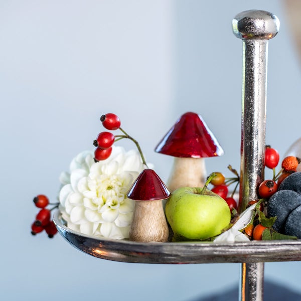 Dekoratives Arrangement auf einer silberfarbenen Etagere mit Pilzfiguren, Hagebutten, einer Dahlie und einem Apfel