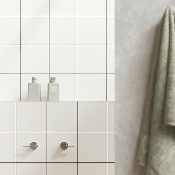 Badezimmerwand mit quadratischen Fliesen und Armaturen, inklusive zwei Seifenspendern und einem hängenden Handtuch.