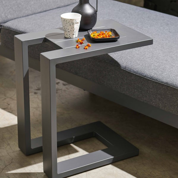 Beistelltisch in C-Form aus Metall an einer grauen Gartenlounge mit Tasse und Vase.