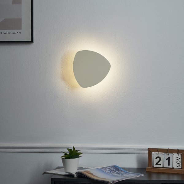 Moderne Wandleuchte in einem hellen Raum mit Tisch und Dekoration.