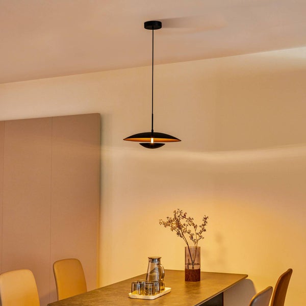 Moderne Pendelleuchte in Schwarz und Gold über einem Esstisch in einem hellen, aufgeräumten Raum.