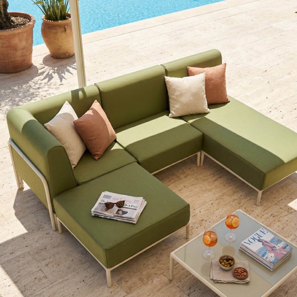 Modernes grünes Garten-Ecksofa mit Hocker und Tisch auf einer hellen Steinterrasse am Pool, dekoriert mit Kissen und Zeitschriften.
