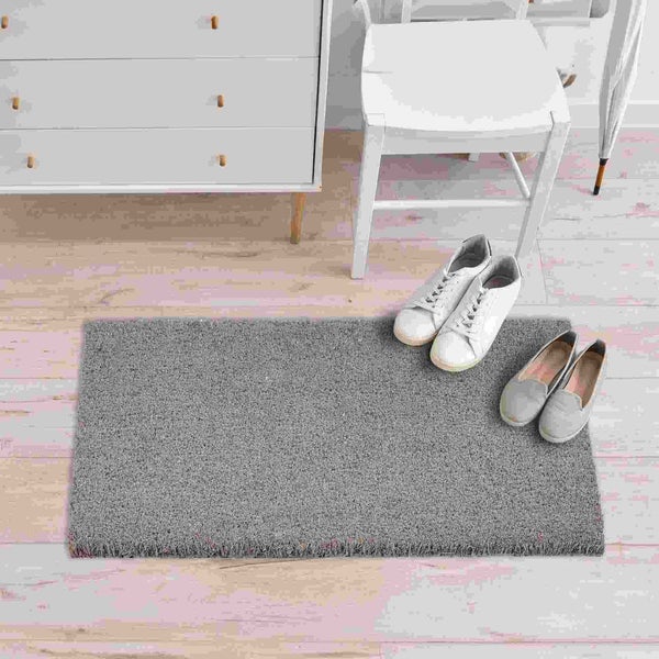 Graue Fußmatte mit Schuhen im Flur vor Kommode und Stuhl.