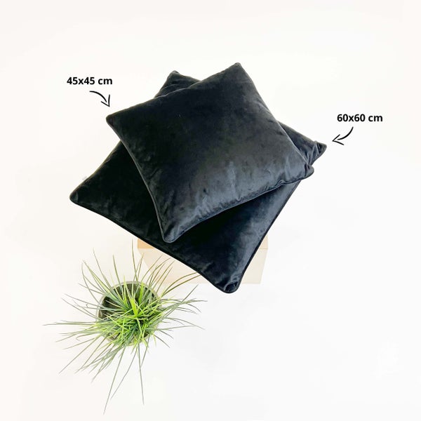 Dekorative Kissen in den Größen 45x45 cm und 60x60 cm auf einem Holzhocker, zusammen mit einer Grünpflanze.