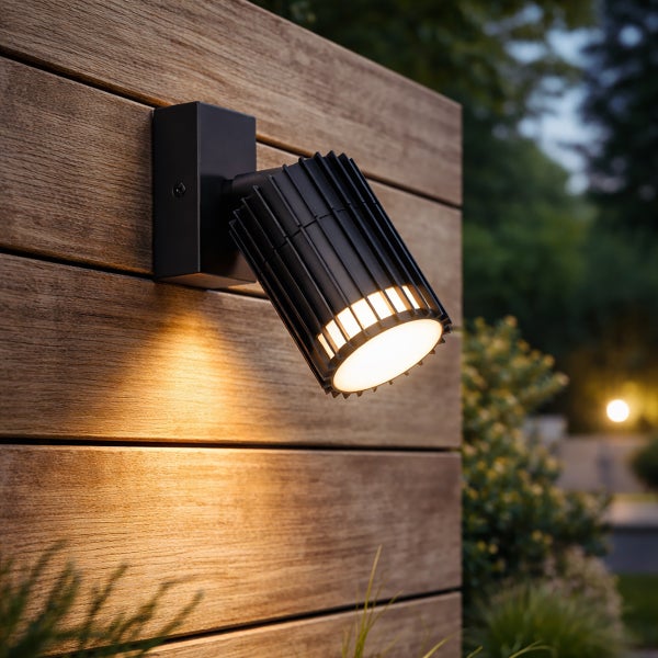 Schwarzer Außenstrahler an einer Holzwand montiert und eingeschaltet.