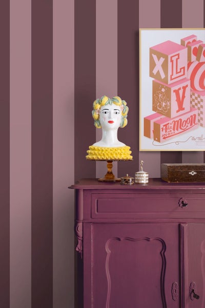 Gestreifte Tapete in Violetttönen an einer Wand hinter einer lila Kommode mit dekorativer Büste und gerahmtem Bild.