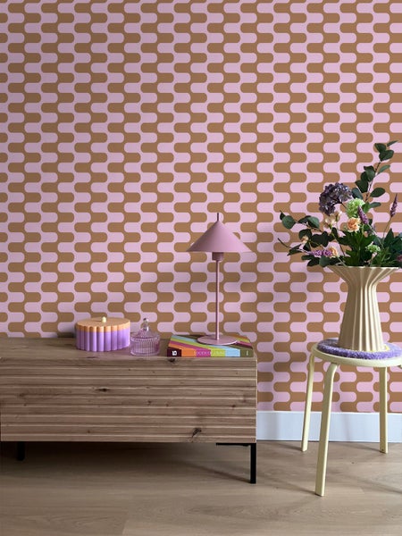 Raumansicht mit gemusterter Tapete, Kommode, Tischlampe und Blumenarrangement auf einem Hocker