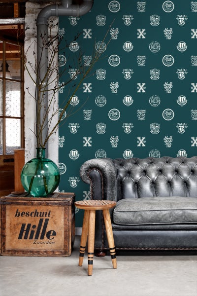 Dekorative Szene mit einer Couch, einem Hocker und einer Holzkiste vor einer Wand mit College-Motivtapete.