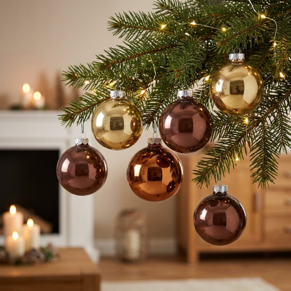 Weihnachtskugeln hängen an einem Tannenbaumzweig mit Lichterkette in einem wohnlich eingerichteten Zimmer mit Kamin