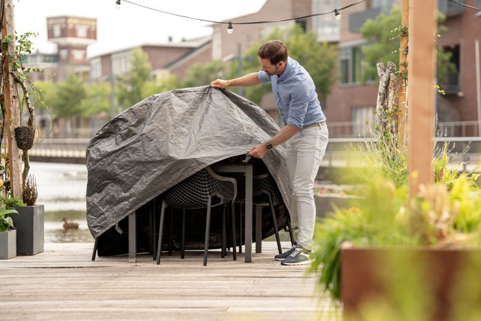 Mann legt eine Schutzhülle über eine Gartentischgruppe im Außenbereich.