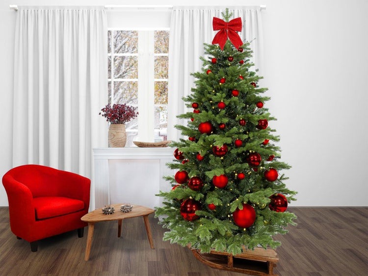 Künstlicher Weihnachtsbaum mit LED Lichterkette und roter Dekoration geschmückt in einem Wohnzimmer mit Sessel auf einem Holzschlitten stehend