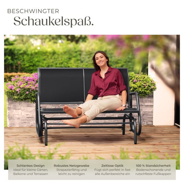 Schwarze Garten-Schaukelbank aus Metall und Netzgewebe auf einer hellen Holzterrasse im Garten mit einer sitzenden Frau.