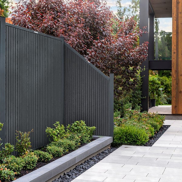 Moderne Sichtschutzwand aus Kunststoff in einem gepflegten Garten mit Pflanzbeet und gepflastertem Weg vor einem modernen Wohnhaus.