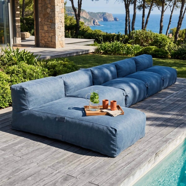 Modernes modulares Outdoor-Lounge-Sofa aus blauem Textil auf einer Holzterrasse an einem Pool mit weitem Meerblick.