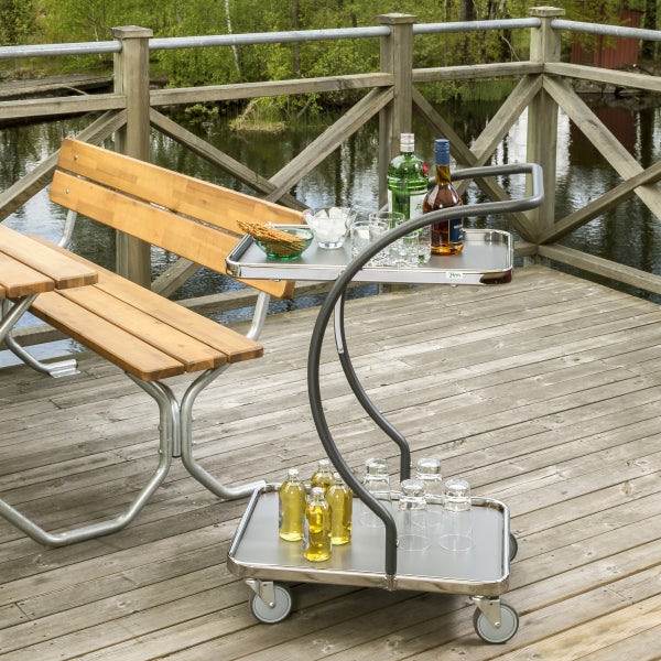 Servierwagen mit Getränken und Snacks neben einer Picknickbank auf einer Holzterrasse.