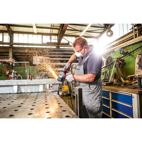 Ein Handwerker nutzt einen Winkelschleifer an einem Metallwerkstück in einer Werkstatt und erzeugt dabei Funkenflug.